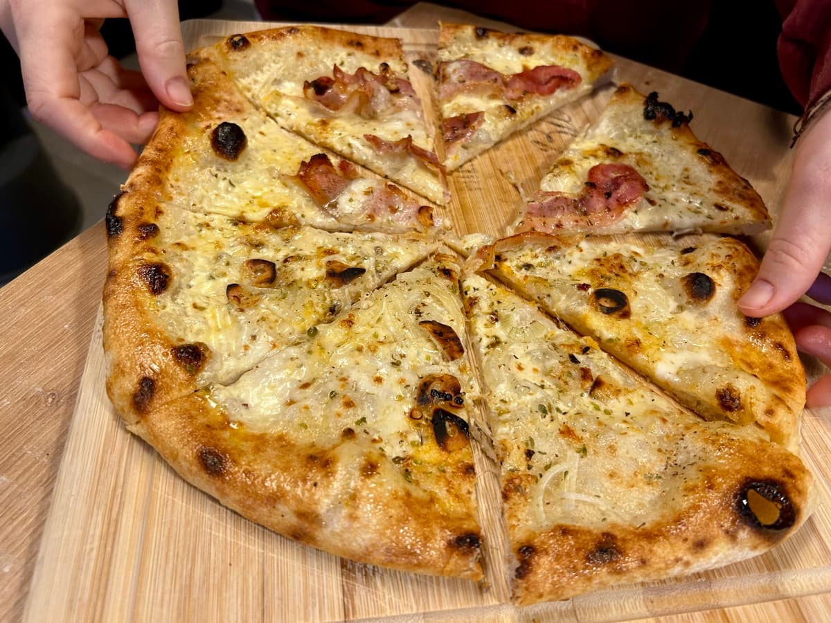 Hände greifen nach frischen Pizzastücken
